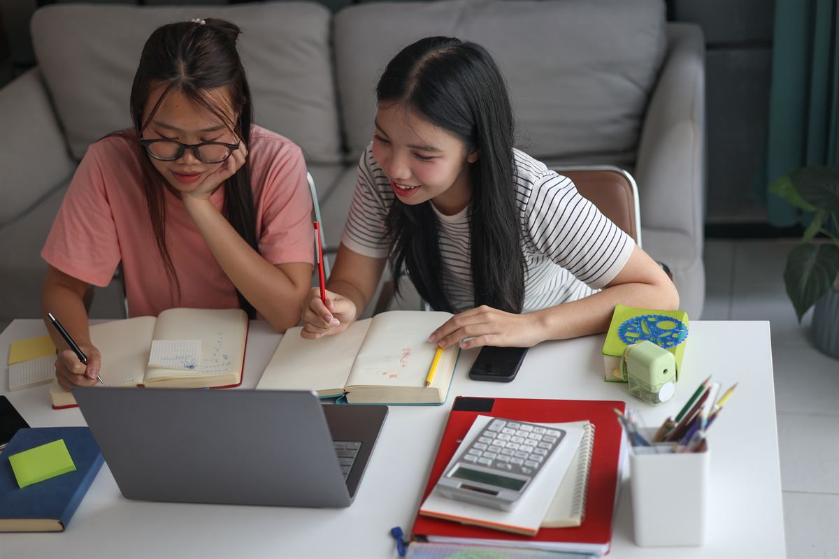 Two students studying together at a table with open notebooks and a laptop.