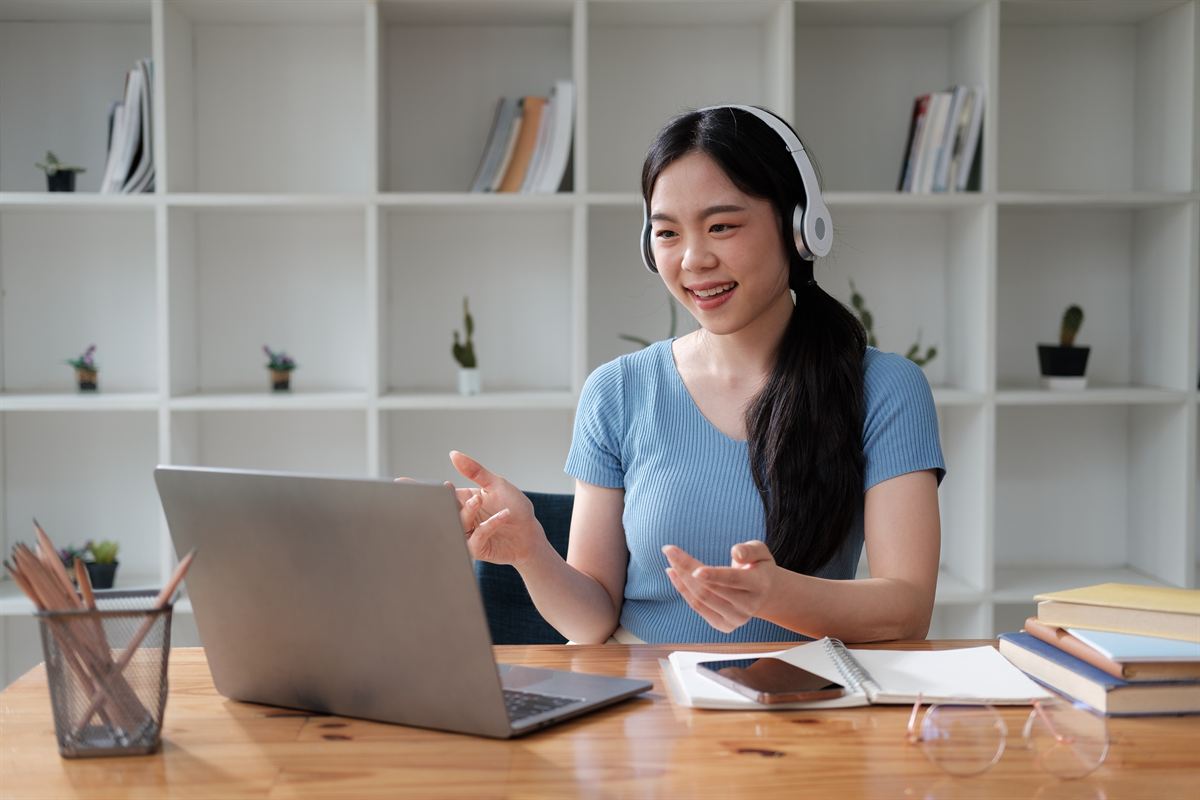 A student wearing headphones smiling during an online video session at a laptop.