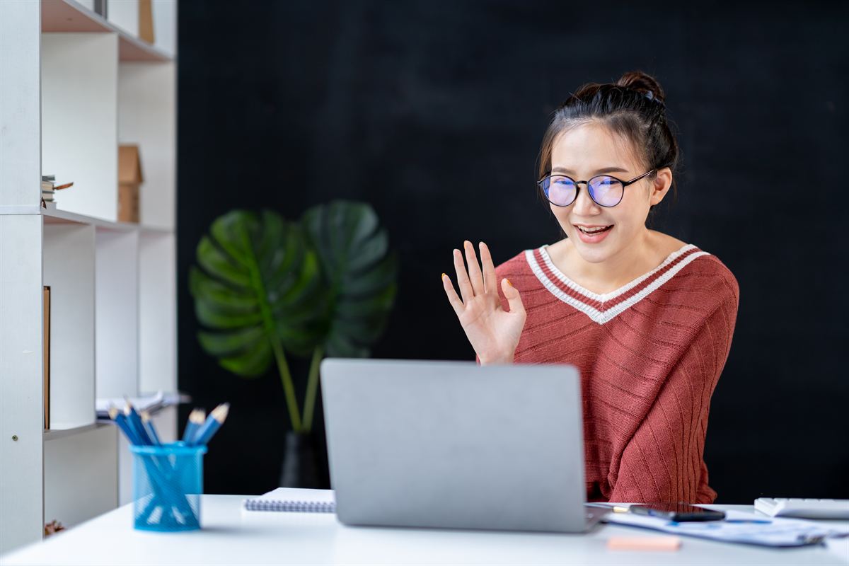 A volunteer in glasses waving hello at her laptop during an online video call.