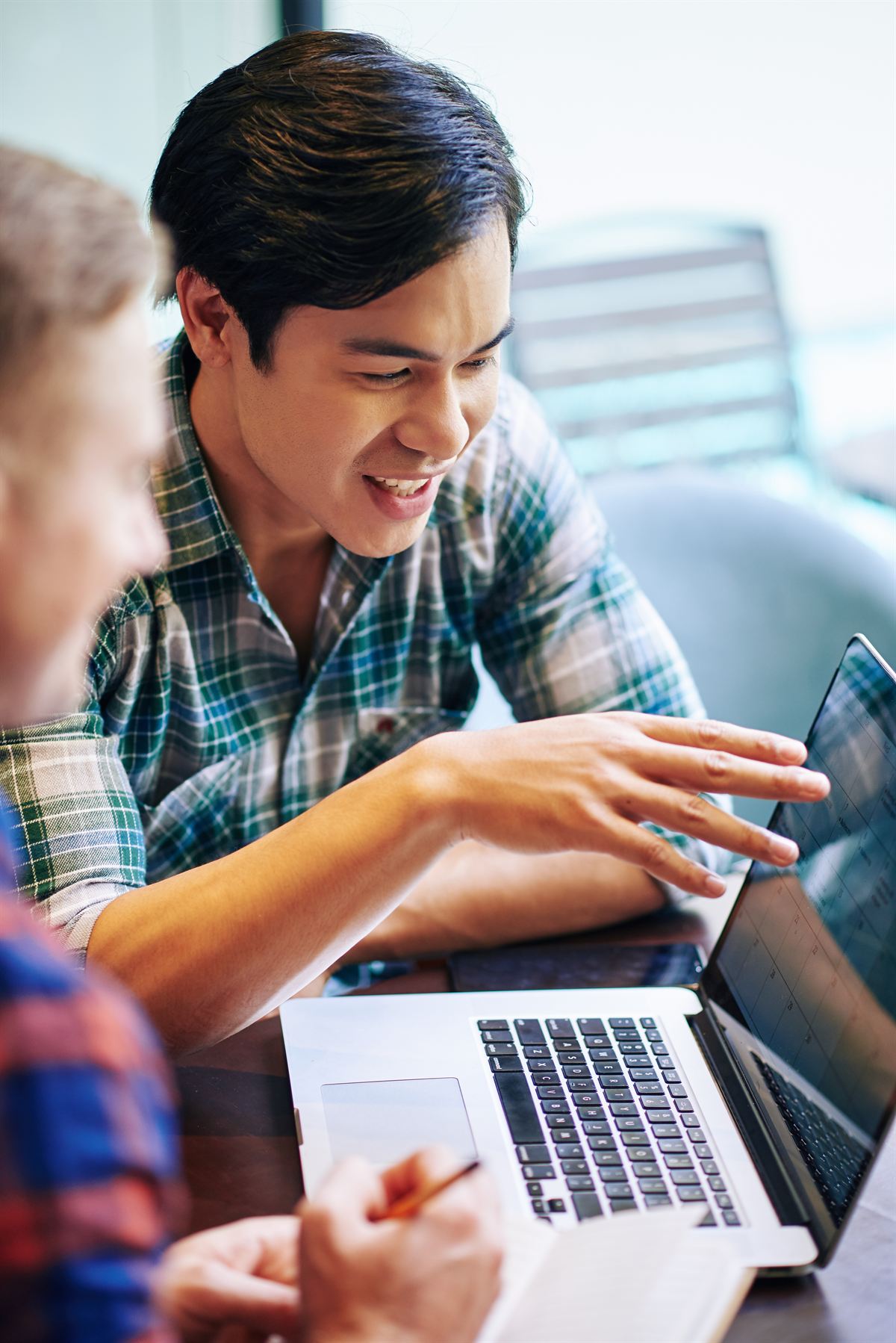 A smiling tutor pointing at a laptop screen, walking another person through it.
