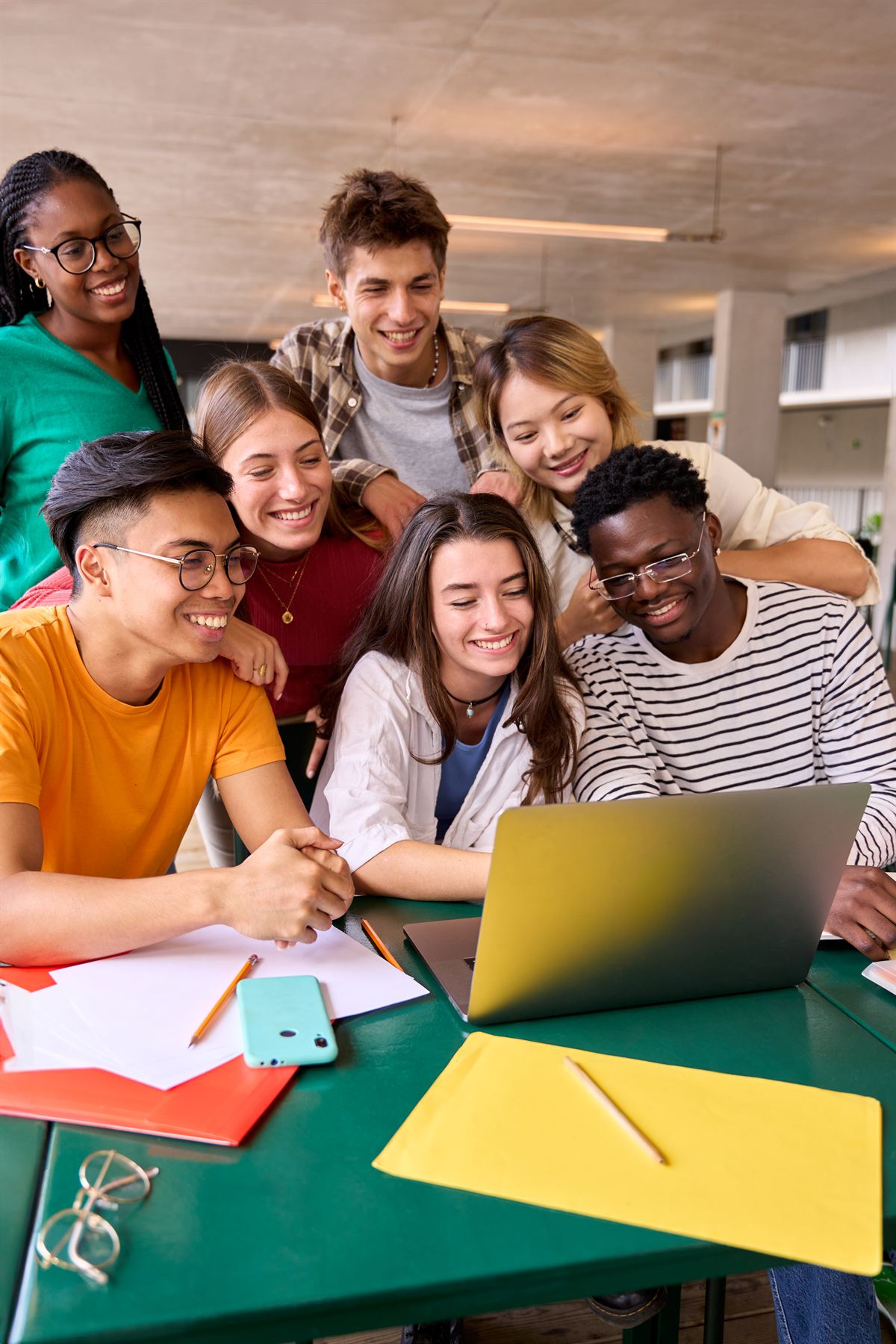 A diverse group of students gathered around a laptop, smiling together.